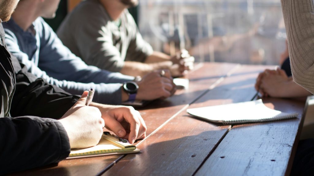 Group of coworkers sat at a wooden table with pens and notepads.